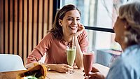 Eine junge Frau hockt an einem Tisch und redet mit einer anderen Person