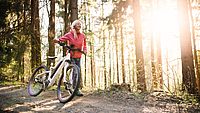 Ältere Frau mit einem E-Bike im Wald
